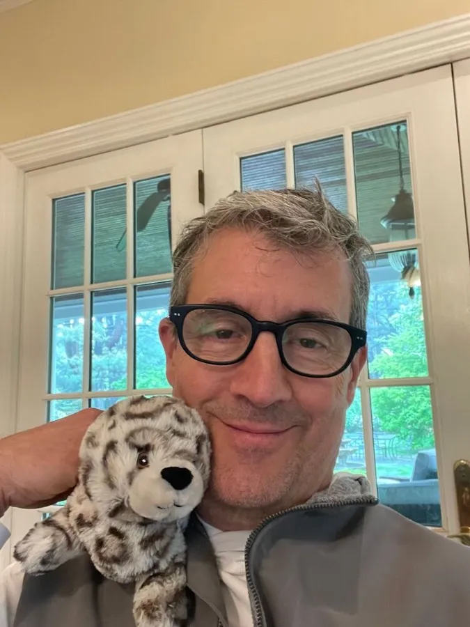 Christopher smiling in LOOK OPTIC Bond readers with a plush snow leopard on his shoulder