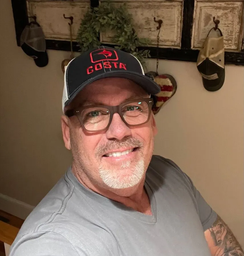 Christopher smiling in LOOK OPTIC Cosmo readers and a baseball cap