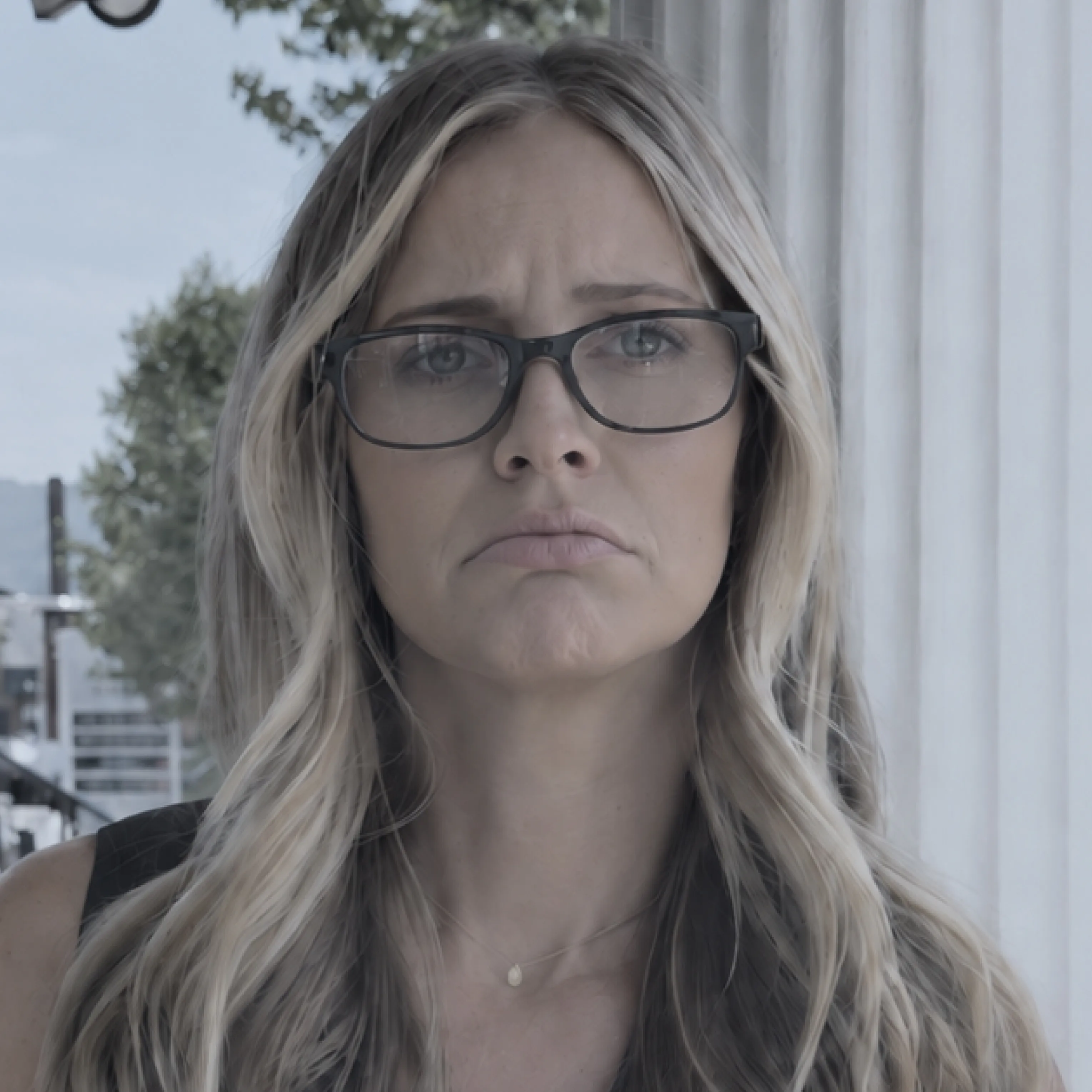 A woman outdoors wearing plain black rectangular readers, looking unimpressed