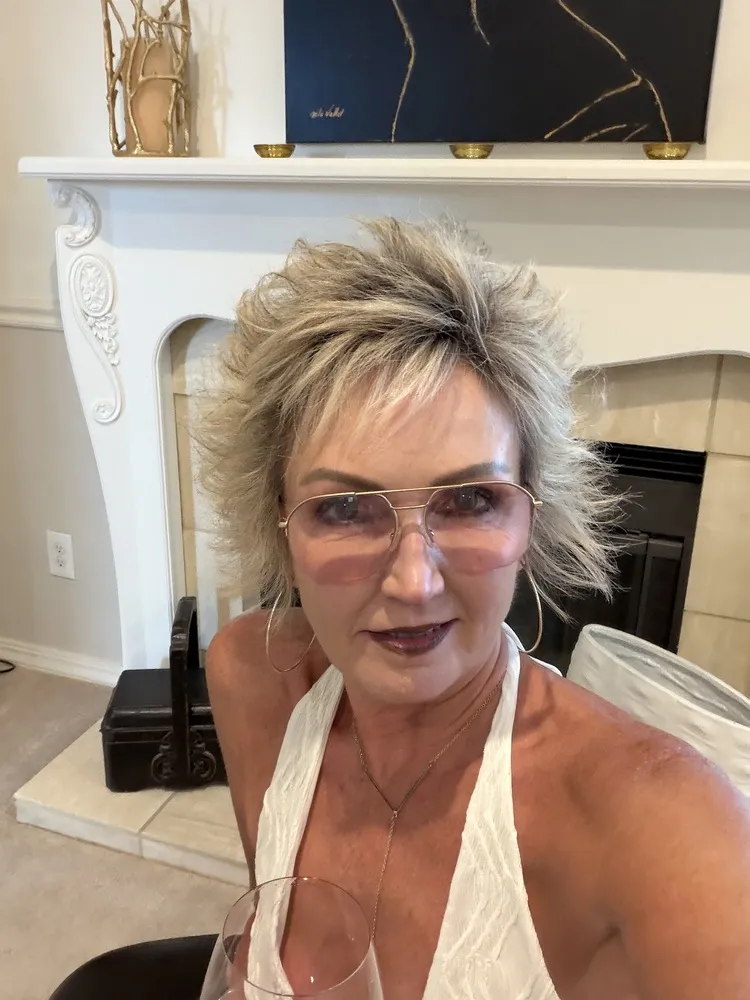Janeen wearing LOOK OPTIC Muse readers, standing in front of a fireplace
