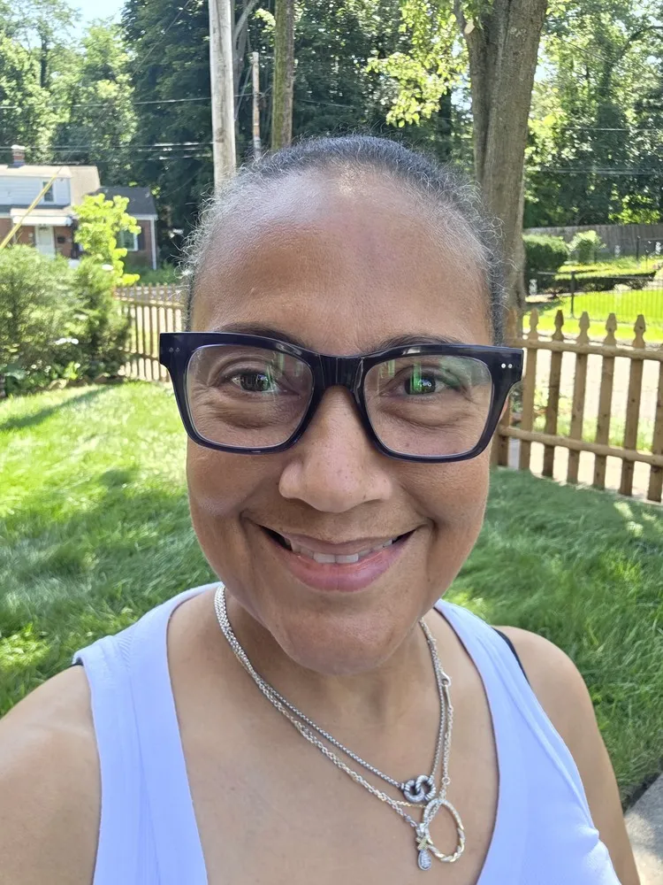 Sharon wearing LOOK OPTIC Cosmo Progressives with dark frames, outdoors in a garden